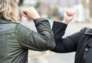 Two women in over coats bump elbows.