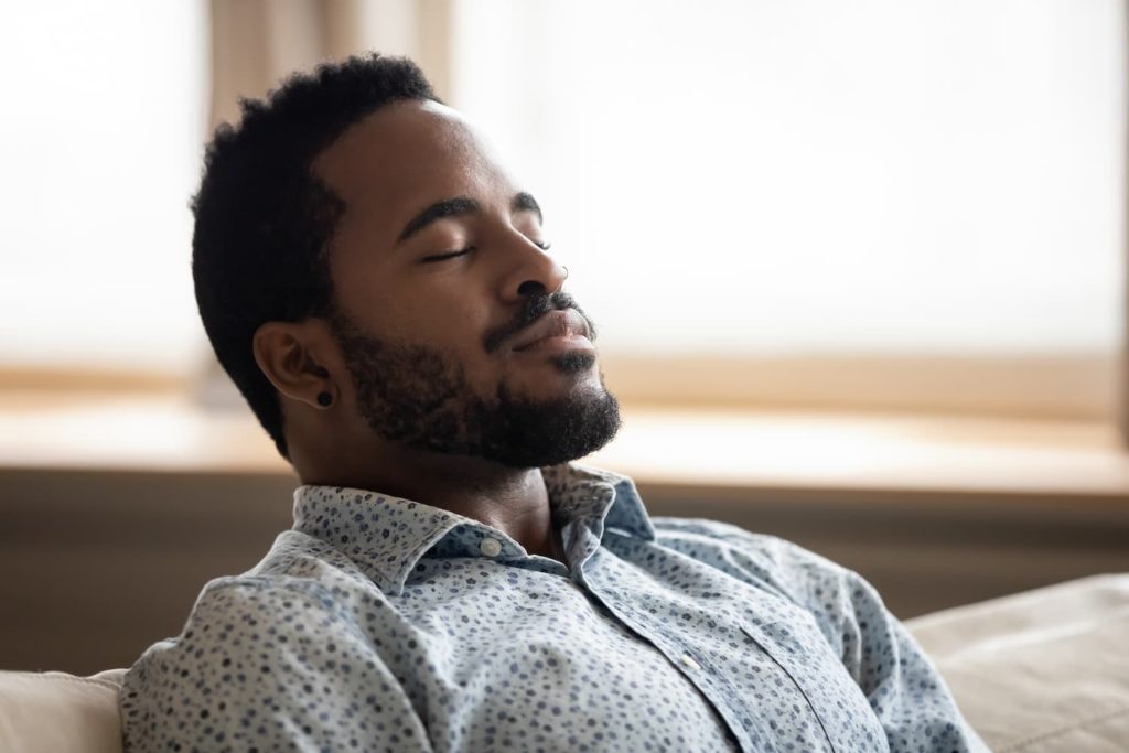 Black man reclines with eyes closed.
