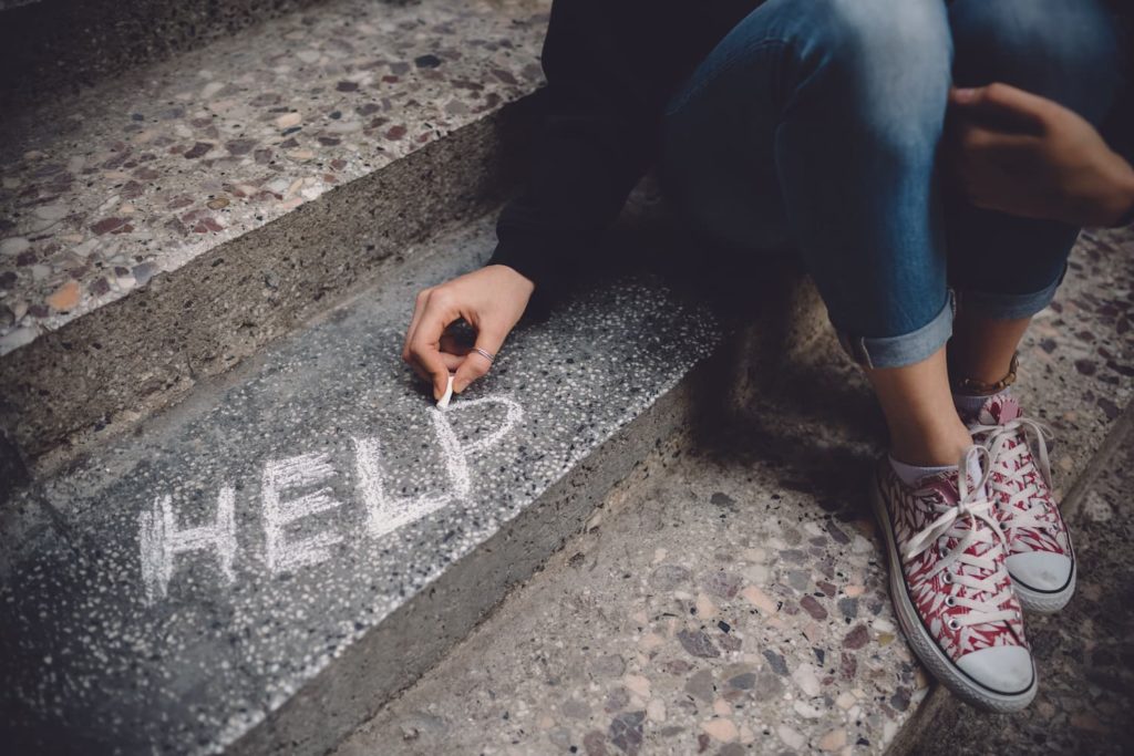 Woman writes the word help on concrete steps.